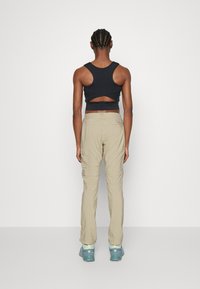 Schwarzes kurzgeschnittenes Oberteil mit ausgeschnittenem Rücken, kombiniert mit hellbeigen Cargo-Hosen. Das Outfit verfügt über praktische Taschen und strukturierte Stoffe.