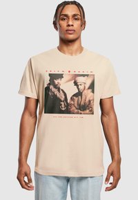 Beige bomulds t-shirt med et forsidegrafik af to mænd i sort-hvid med rød tekst "ERIC B. & RAKIM" og "LET THE RHYTHM HIT 'EM."