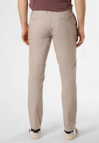 Beige trousers with a slim fit, featuring two back pockets with buttons and a smooth, textured fabric. Worn with light-colored sneakers.