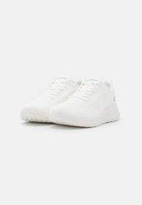 White athletic shoes with a textured mesh upper, thick sole, and light blue accents on the logo. Laced with flat white laces.