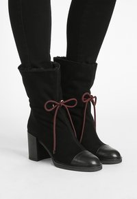 Black fabric ankle boots with a heeled sole, featuring a pointed toe, black leather cap, and a burgundy ribbon for closure.