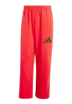 Pantaloni della tuta rossi realizzati in tessuto morbido, con vita elasticizzata e un logo a tre strisce nere sulla gamba sinistra.