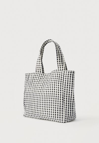 Τσάντα από ύφασμα με ασπρόμαυρο καρό μοτίβο και κοντά λουριά ώμου, σε απλό φωτεινό φόντο.
