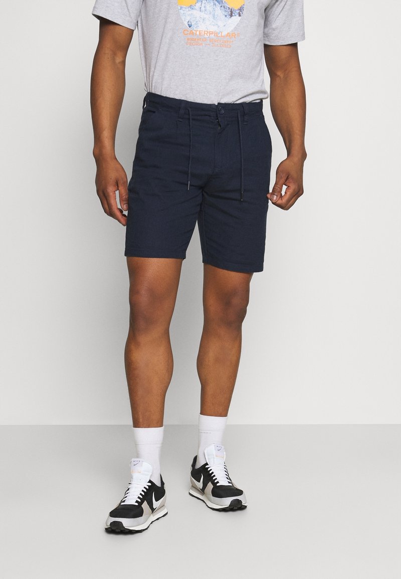 Navyblauwe shorts van lichtgewicht stof, met een verstelbare elastische tailleband, zakken en een relaxte pasvorm, gecombineerd met een grijs graphic t-shirt.