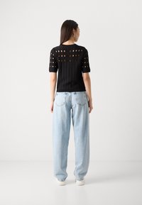 Black ribbed knit top with circular cut-outs on sleeves and back, paired with light blue high-waisted jeans and white sneakers.