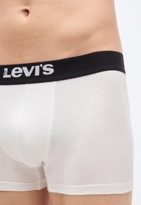 Valkoiset puuvillaiset bokserialushousut, joissa musta elastinen vyötärönauha ja "Levi's"-logo. Sileä pinta ja vartaloa myötäilevä muotoilu.