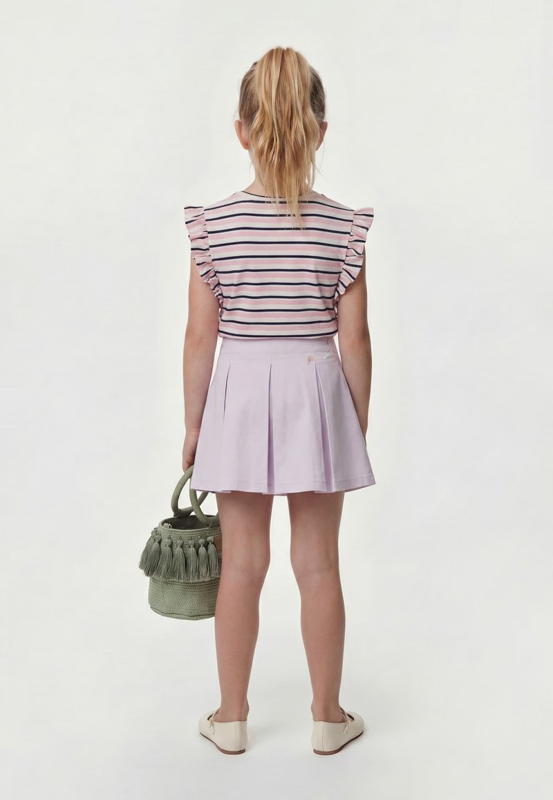 Fille avec une queue de cheval claire portant un top rayé à manches à volants et une jupe lilas plissée, tenant un sac à main vert à pampilles, debout de dos.