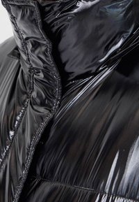 Černá bundová pufferka s lesklým povrchem, s vysokým límcem, prošívanými detaily a prošívanou strukturou. Zapínání na zip vpředu.