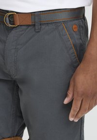 Gray pants with a smooth texture, featuring a brown leather belt and orange accent stitching. Includes a button and side pockets.