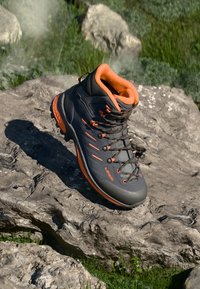 Grauer Wanderschuh mit orangen Akzenten, strukturiertem Obermaterial und einer robusten Sohle. Verfügt über auffällige Schnürsenkel und einen gepolsterten Schaft für zusätzlichen Komfort.