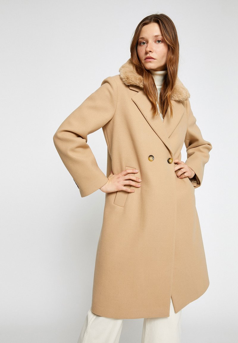 Beige wollen mix jas met een bontkraag, dubbelzijdige sluiting en zijzakken; heeft een getailleerd ontwerp en een licht uitlopende zoom.