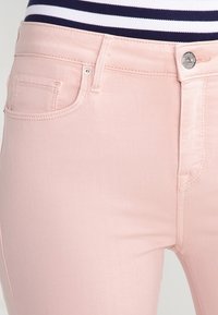 Jeans rosa claro hechos de denim, con un bolsillo frontal, un botón de metal y costuras reforzadas a lo largo de las costuras.