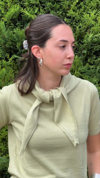 Vihreä neulepusero, jossa on solmittu huiviyksityiskohta kaulassa. Lyhyet hihat ja sileä pinta. Hopeiset renkaat korvakorut täydentävät asua.