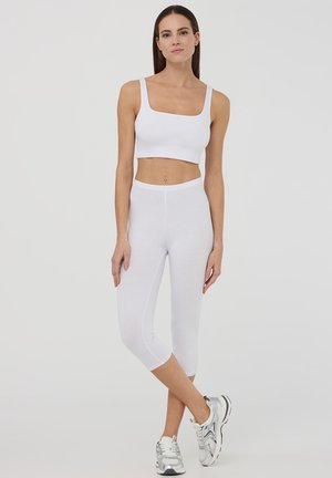 Biały top na krótki rękaw z kwadratowym dekoltem, w zestawie z białymi legginsami sięgającymi do połowy łydki. Materiał jest gładki, z minimalnymi szwami i dopasowany do ciała.