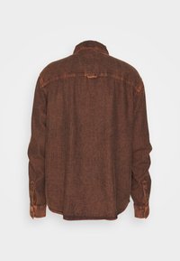 Brun denimskjorta med avslappnad passform, långa ärmar och knäppte manschetter. Har en klassisk krage och en subtilt texturerad tyg.