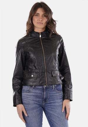 Giacca di pelle nera con colletto alto, chiusura con zip frontale, due tasche anteriori e finitura testurizzata. Abbinata a jeans blu.