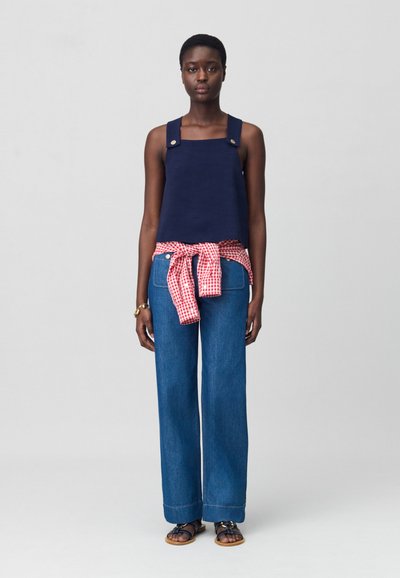 Top corto navy con bretelle larghe, abbinato a jeans azzurri larghi e una camicia a quadri rossi legata in vita. Sandali marroni indossati.