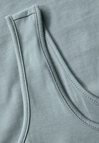 Vaaleansininen hihaton paita, jossa on ribattua tekstuuria, pyöreä pääntie ja kontrastiväriset tikkausreunat.