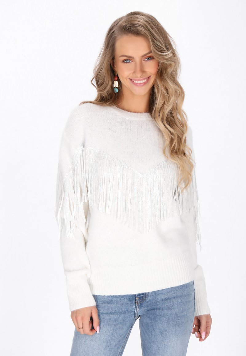 Maglione bianco con un design a frange a forma di V, tessuto morbido e polsini a coste. Abbinato a jeans blu.