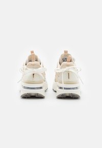 Zapatilla de color neutro con una parte superior texturizada, cuello acolchado y una suela gruesa que presenta un cojín de aire visible. Los cordones están atados de manera ordenada, vista desde atrás.