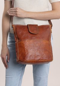 Brun läderaxelväska med lockstängning, med en strukturerad yta, framficka och justerbar rem. Enkel rektangulär design.