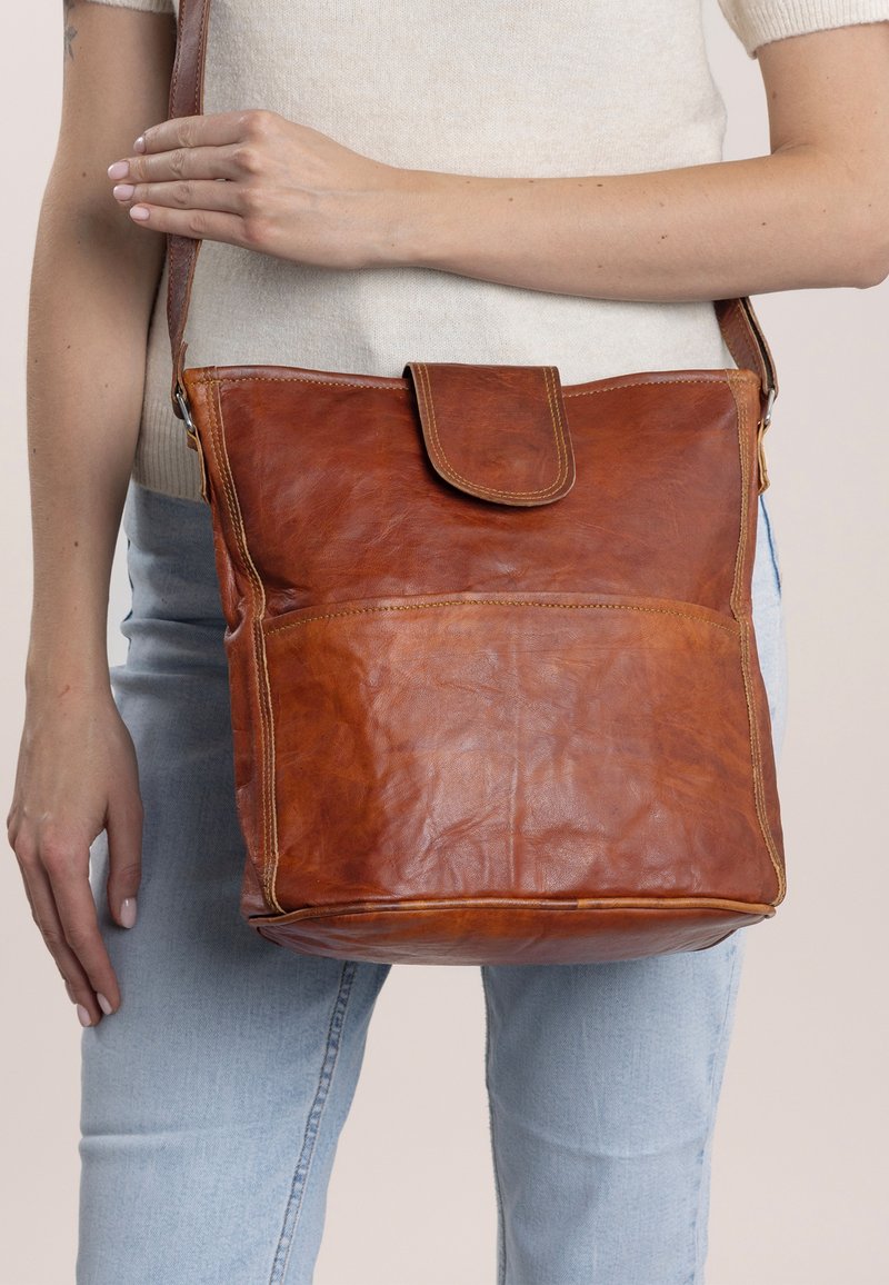 Brun läderaxelväska med lockstängning, med en strukturerad yta, framficka och justerbar rem. Enkel rektangulär design.