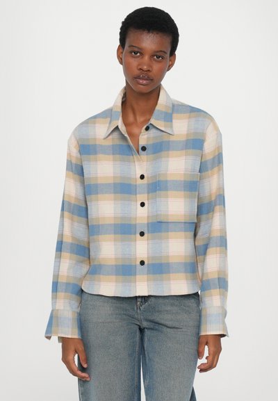 Rutete flanellskjorte i blått, beige og rosa med brystlomme, knappestolpe foran og oppbrettede lange ermer. Bært med blå jeans.