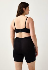 Mustat bralette-toppit, joissa on säädettävät olkaimet ja hakasuljenta, yhdistettynä mustiin keskipituisiin shortseihin. Sujuva kangas, jossa on tyylikäs ja minimalistinen muotoilu.