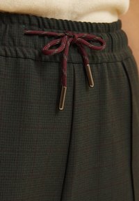 Green plaid trousers with an elastic waistband, featuring a maroon drawstring with metal tips and a textured fabric.