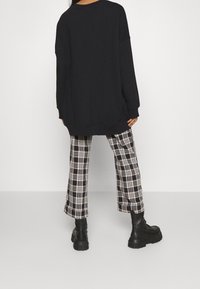 Sudadera negra de gran tamaño con mangas largas, combinada con pantalones de pierna ancha con cuadros en negro y blanco y botas negras gruesas.