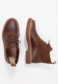 Botas de tobillo de cuero marrón y ante con punta redonda, diseño de cordones, suela de goma y costuras en contraste. Parte superior texturizada con una lengüeta.