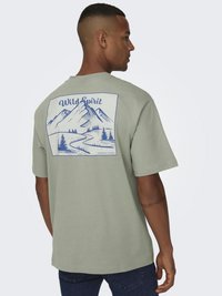 Lichtgroene t-shirt met korte mouwen met een grafische weergave van een blauwe berglandschap en de tekst "Wild Spirit" op de achterkant.