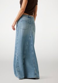 Gonna maxi in denim blu chiaro con una forma svasata, caratterizzata da una vita alta, tasche posteriori e dettagli cuciti lungo le cuciture.