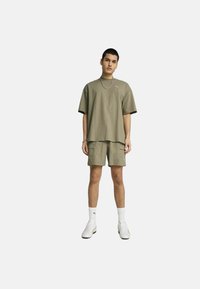 Kaki oversize majica s kratkim rukavima, u kombinaciji s odgovarajućim cargo kratkim hlačama. Bijele tenisice i čarape do gležnja upotpunjuju izgled.