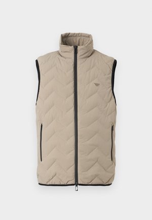 Bež prsluk bez rukava s visokim ovratnikom, crnim patentnim zatvaračem u sredini, dva bočna džepa na patentni zatvarač i suptilnim uzorkom cikcak šava.