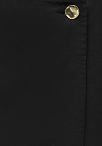 Gros plan d’un tissu noir avec un seul bouton doré brillant et une boutonnière sur le côté droit.