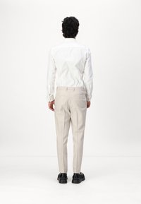 Weißes Hemd mit langen Ärmeln, kombiniert mit hellbeigen Hosen und schwarzen Schuhen; sichtbare Rückendetails umfassen Taschen und eine taillierte Passform.