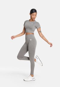 Sivina športna zbirka, ki vključuje prilagojen cropped top in visok pas na leggingih. Material ima teksturiran zaključek. Bele logotipne akcenti na obeh kosih.