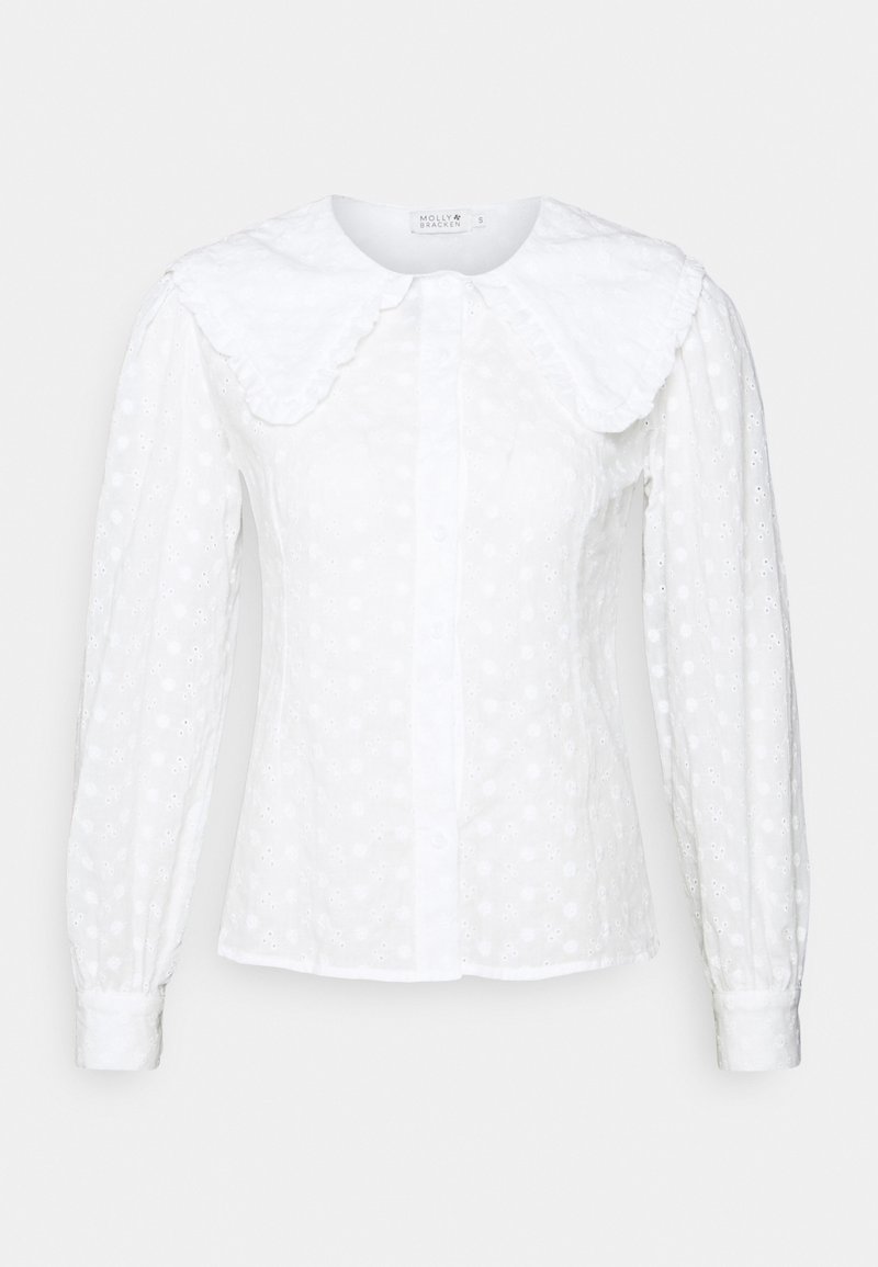 Blouse blanche à manches longues avec grand col festonné et motif floral en ajouré subtil, fermeture à boutons sur le devant, et taille cintrée.