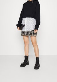 Sudadera corta negra con una capa inferior blanca con patrón, combinada con una falda de patrón en blanco y negro. Botas de combate negras y un pequeño bolso negro.