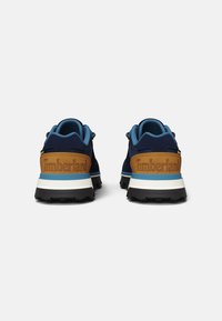 Zapatillas Timberland en azul marino y marrón con tela texturizada, cuellos acolchados y medias suelas blancas; cuentan con un logo en la parte trasera y acentos en azul contrastante.