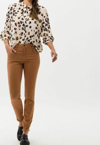 Blusa de estampado de leopardo con cuello abotonado, combinada con pantalones marrones ajustados y mocasines negros. Tejido suave con mangas enrolladas y bolsillos frontales.