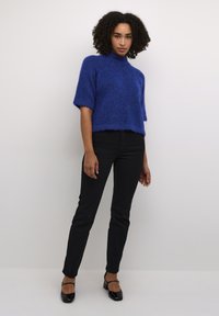 Blauer, flauschiger Kurzarmpullover mit Stehkragen, kombiniert mit schwarzen Slim-Fit-Hosen und schwarzen High Heels. Die Textur wirkt weich und gemütlich.