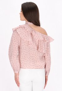 Bluse mit pinken Punkten, die ein asymmetrisches Rüschendesign, offene Rückseite, lange Ärmel und geknöpfte Manschetten aufweist.