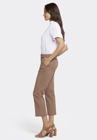 T-shirt blanc à manches courtes associé à un pantalon cropped marron avec poches latérales et une texture douce. Des sandales à talons marron complètent la tenue.