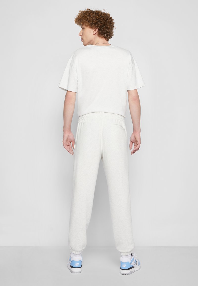 T-shirt blanche à col rond et manches courtes associée à un jogging léger gris clair avec taille élastique. Tissu texturé, coupe décontractée et poignets côtelés.