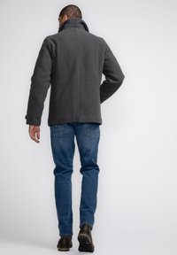 Palton gri din lână cu guler înalt, având o croială lejeră. Asortat cu blugi albaștri din denim și cizme negre, văzut din spate.