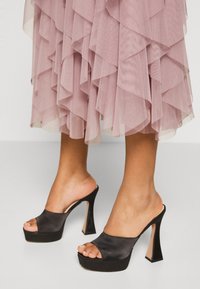 Talons plateformes noirs en satin avec une ouverture à l'avant et un talon épais. Le design présente une silhouette élégante et une finition brillante.