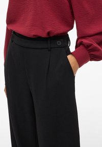 Hochtaillierte schwarze Hose mit Falten, ausgestattet mit einer glatten Textur, seitlichen Taschen und einem Zwei-Knopf-Verschluss am Bund.