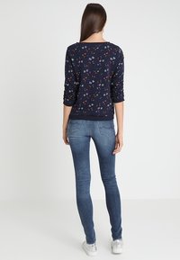 Felpa navy con motivo floreale, maniche lunghe, polsini a coste e scollatura rotonda, abbinata a jeans slim-fit blu e sneakers bianche.